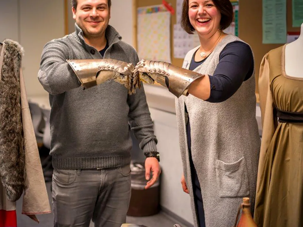Zwei Erwachsene zeigen einen Ritterhandschuh aus Metall.